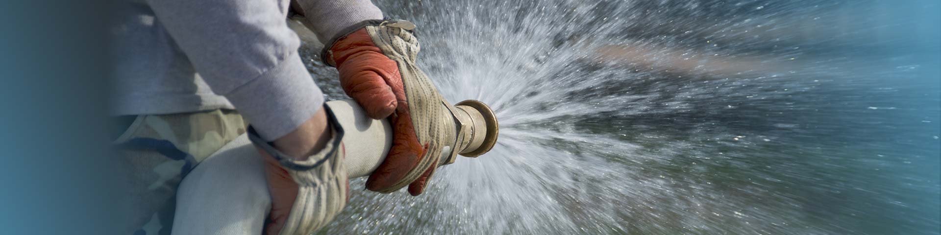 Zwei Hände halten einen Wasserschlauch aus dem Wasser spritzt. 